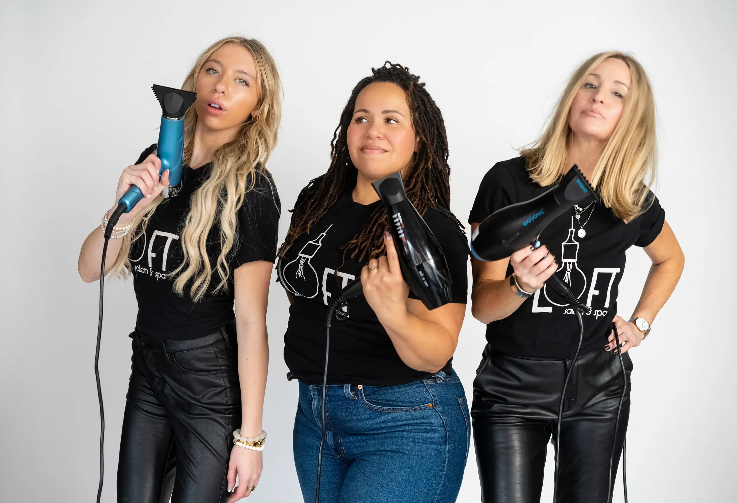 Three Loft stylists posing with blow dryers on their shoulders